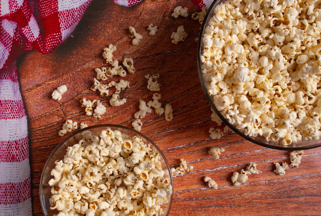 Two bowls of popcorn on a tale with loose popcorn around.