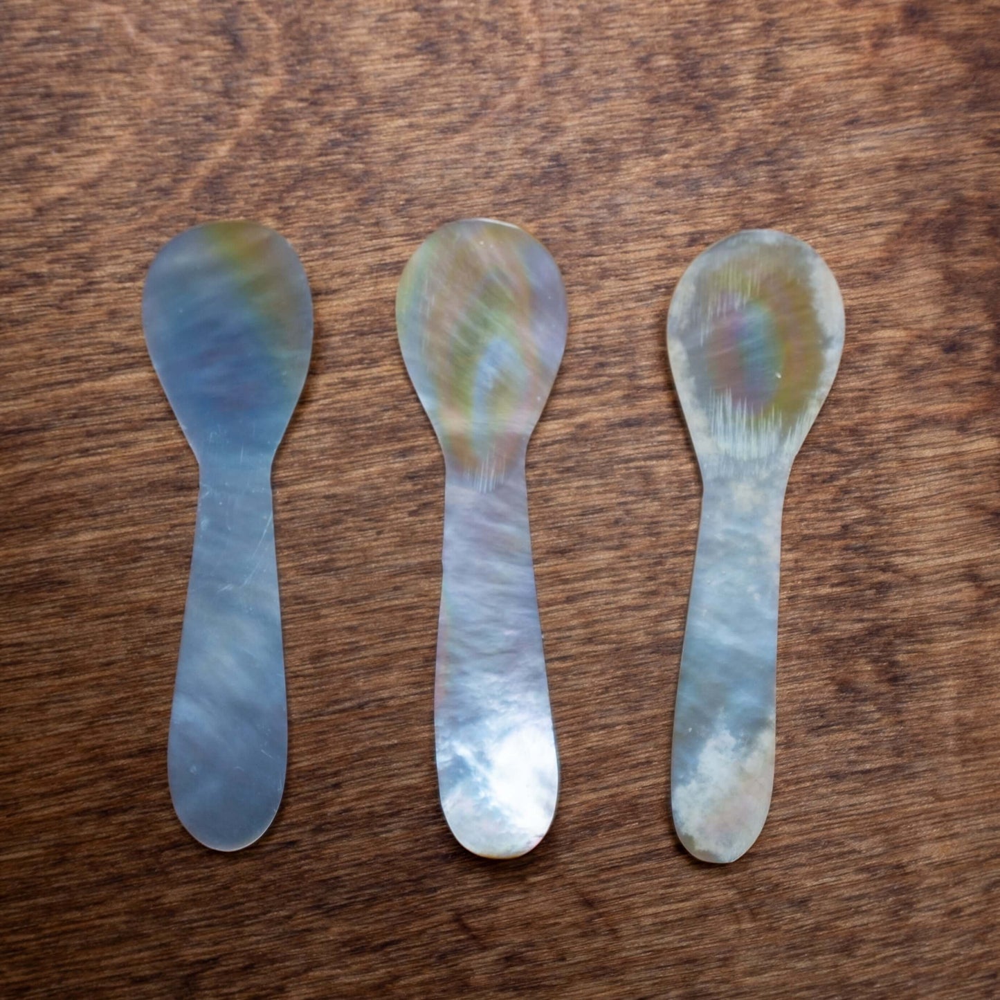 Set of 3 mother of pearl caviar spoons placed on a wooden table.