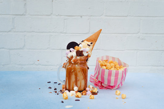 Small pink paper bag of popcorn with an elaborate ice cream sundae next to it.