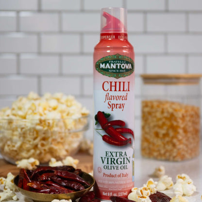 Spray bottle of chili pepper infused olive oil, with chili peppers, popcorn kernels, and popped popcorn.