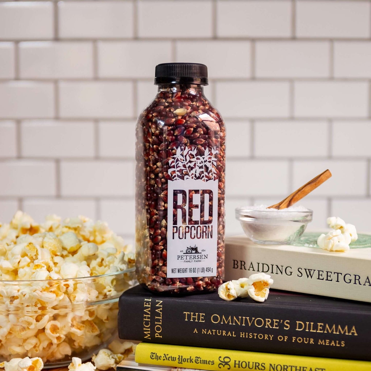 Red popcorn kernels by Petersen Family Farm. 16oz Plastic bottle on counter with popcorn